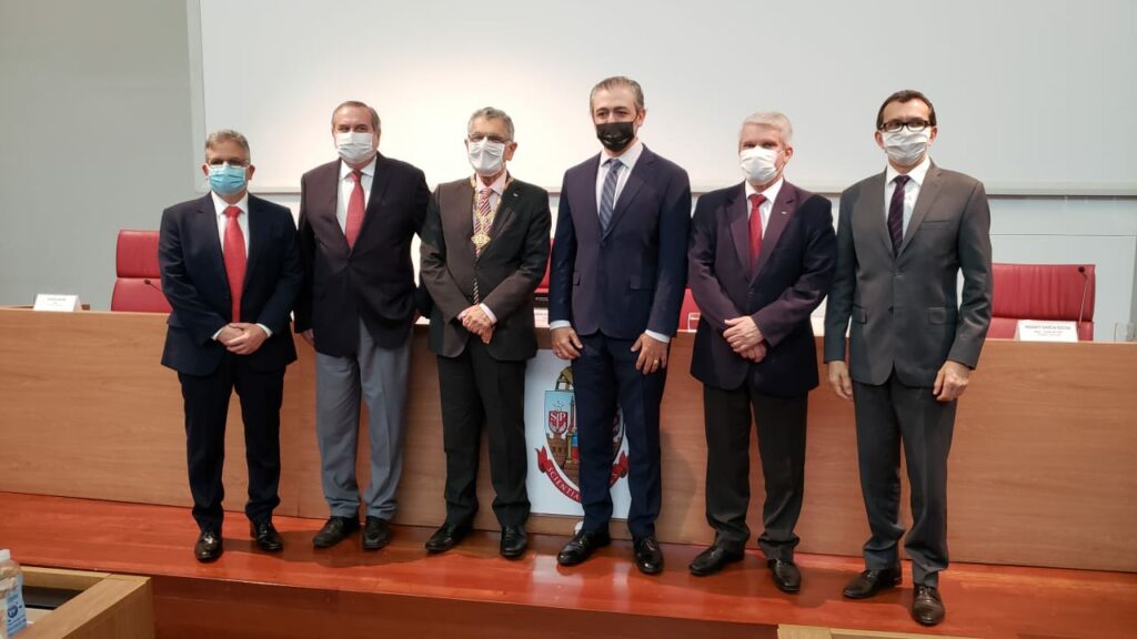 Foto do empossamento da Nova Diretoria da FOUSP para o Quadriênio 2021-2025. A fotografia foi realizada no Auditório do Conselho Universitário onde todos os presentes estão usando máscaras faciais. Da direita para esquerda temos o Prof. Dr. Giulio Gavini - Novo Diretor da FOUSP usando terno com gravata vermelha, Prof. Dr. Rodney Rocha - Ex-Diretor da FOUSP vestindo terno e de gravata vermelha, Prof. Dr. Marco Antonio Zago - Reitor da USP usando terno e gravata listrada em branco e vermelho, Prof. Dr. Giuseppe Romito - Vice-Diretor da FOUSP usando terno e gravata listrada azul e cinza